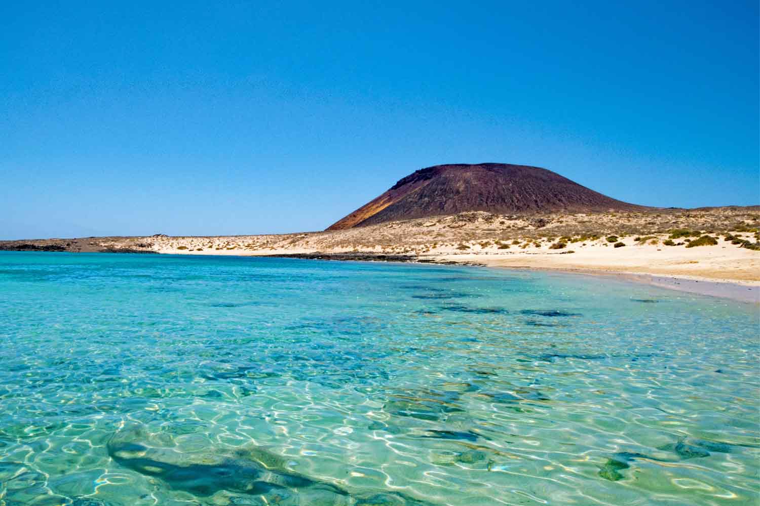 white sandy beach and turquoise water with volcano behind in la graciosa